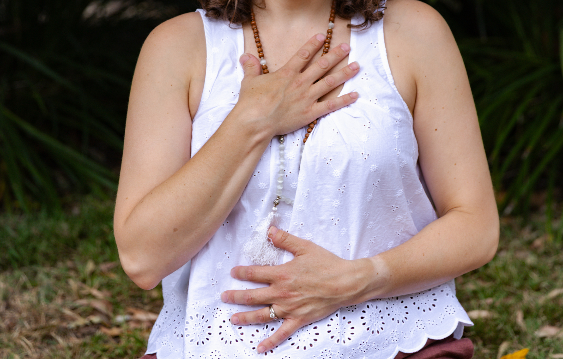 Erin with hands on heart and belly in a grounding meditation pose, wearing mala beads at Beautiful Yoga Melbourne