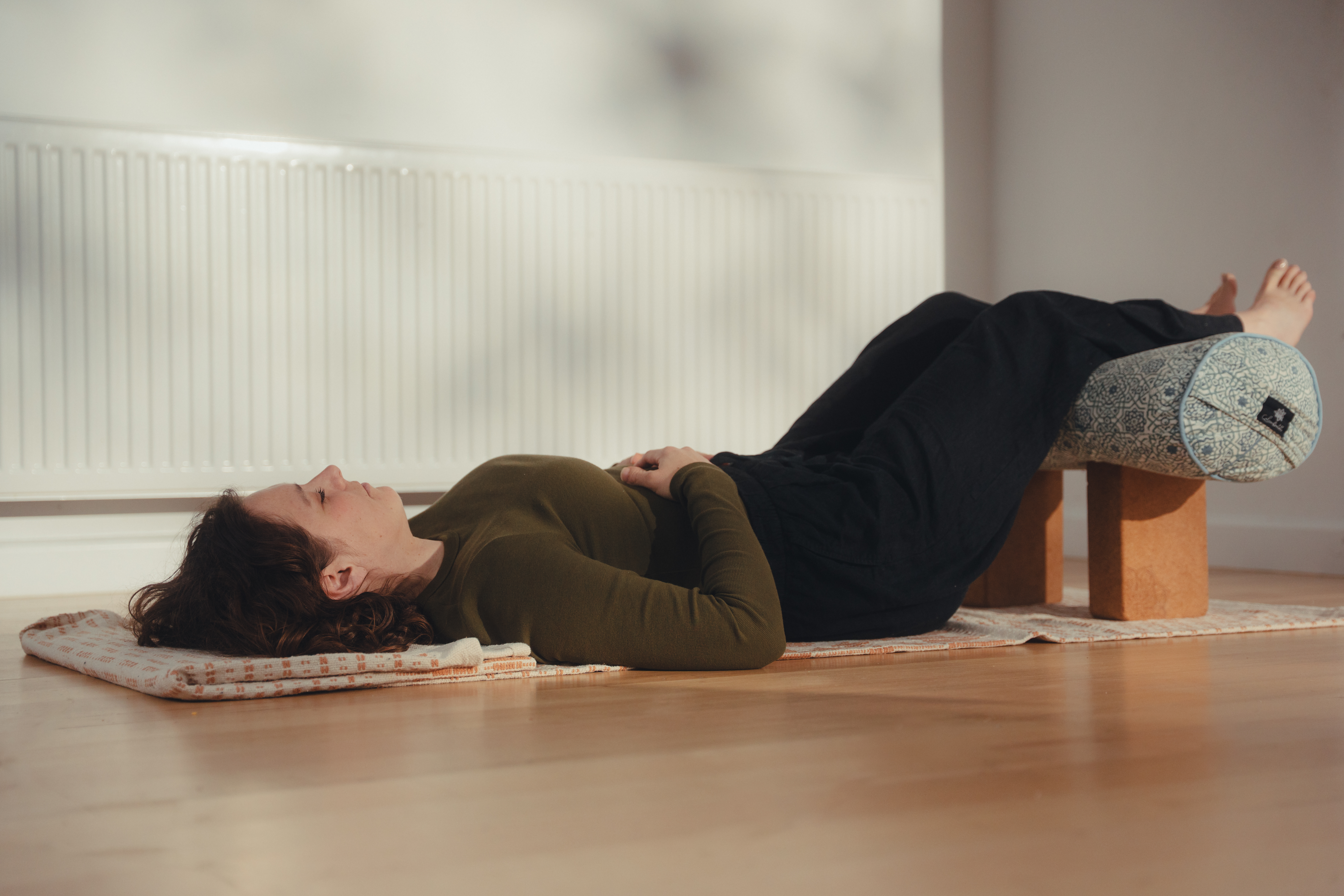 Peaceful restorative yoga pose with legs supported on bolster, demonstrating the deep rest practice
