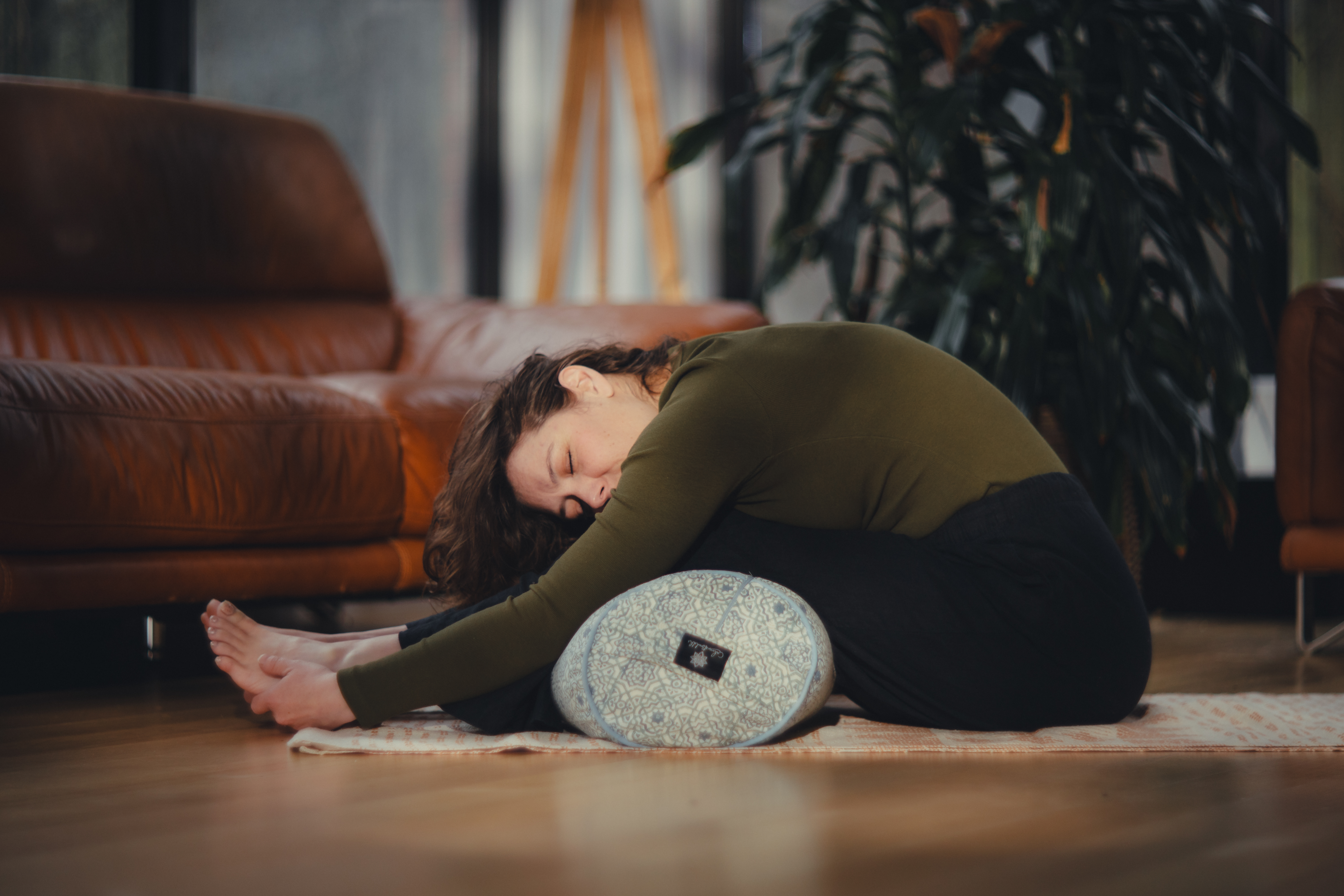 Peaceful forward fold with decorative bolster in warm home setting at Beautiful Yoga